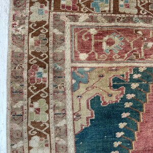 May include: Close-up of a section of a vintage rug with a detailed, ornate design. The rug features a palette of muted colors, including shades of red, blue, beige, and brown. The intricate patterns and textures are visible, showcasing the rug's craftsmanship.