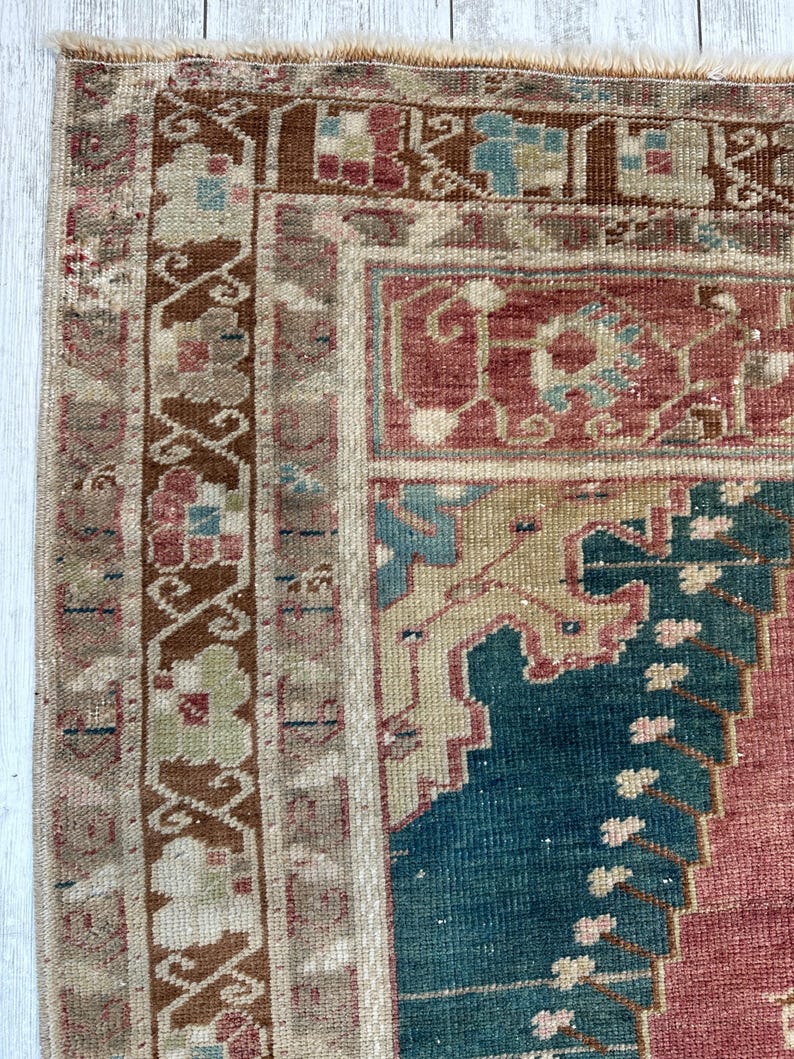 May include: Close-up of a section of a vintage rug with a detailed, ornate design. The rug features a palette of muted colors, including shades of red, blue, beige, and brown. The intricate patterns and textures are visible, showcasing the rug's craftsmanship.