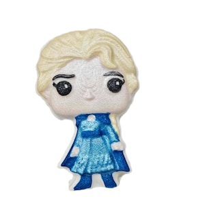 May include: A light-colored, stylized figurine of a character with blonde hair and a blue dress. The figurine has large black eyes and is set against a white background. The figure is likely a collectible or decorative item.