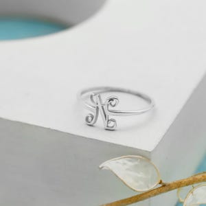Puede incluir: Un anillo de tono plateado que presenta una letra N cursiva y estilizada como punto focal central. La banda es delgada y circular, conect&aacute;ndose con el dise&ntilde;o decorativo de la letra. El metal tiene un acabado liso y pulido que refleja la luz.