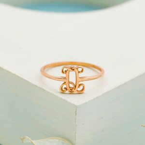 Puede incluir: Un anillo de oro rosa que presenta un elemento decorativo central con forma de letra D, dise&ntilde;ado con un intrincado trabajo de metal en estilo filigrana. La banda es delgada y circular, manteniendo un acabado met&aacute;lico uniforme en toda la pieza.