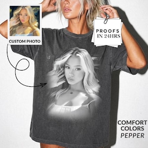 May include: A charcoal grey short-sleeve t-shirt featuring a large black and white photographic print of a person with long hair on the front. The shirt includes a small inset photo labelled CUSTOM PHOTO and a square tag stating PROOFS IN 24HRS.