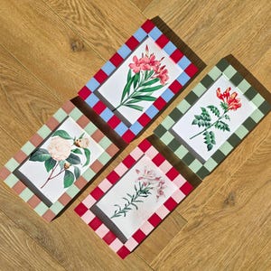 May include: Four rectangular picture frames with floral prints. Each frame has a checkered border in different colours: red and blue, green, pink, and red. The floral prints feature various flowers with green leaves.