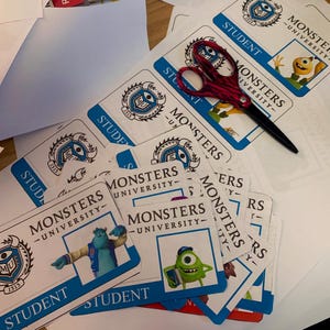 以下が含まれることがあります： モンスターズ・ユニバーシティのロゴと「STUDENT」の文字が印刷された青と白の学生証の束。カードには、映画『モンスターズ・ユニバーシティ』のマイク・ワゾウスキーとサリーの画像が描かれている。
