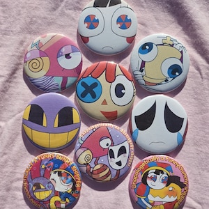 May include: A collection of nine circular pin-back buttons featuring colorful cartoon character illustrations. Designs include expressive faces, abstract shapes, and two buttons with the text Unapologetically a funny gummy shipper.