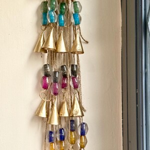 Puede incluir: Adorno colgante decorativo con múltiples hebras de cuerda de yute. Cada hebra tiene un grupo de cuentas de colores y una pequeña campana dorada. Las cuentas son en tonos de rojo, verde, azul, morado y amarillo.