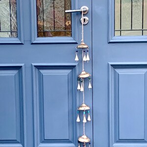 May include: A silver wind chime with five tiers of bells and beads hangs from a door handle. The bells are silver and the beads are blue, green, and white.