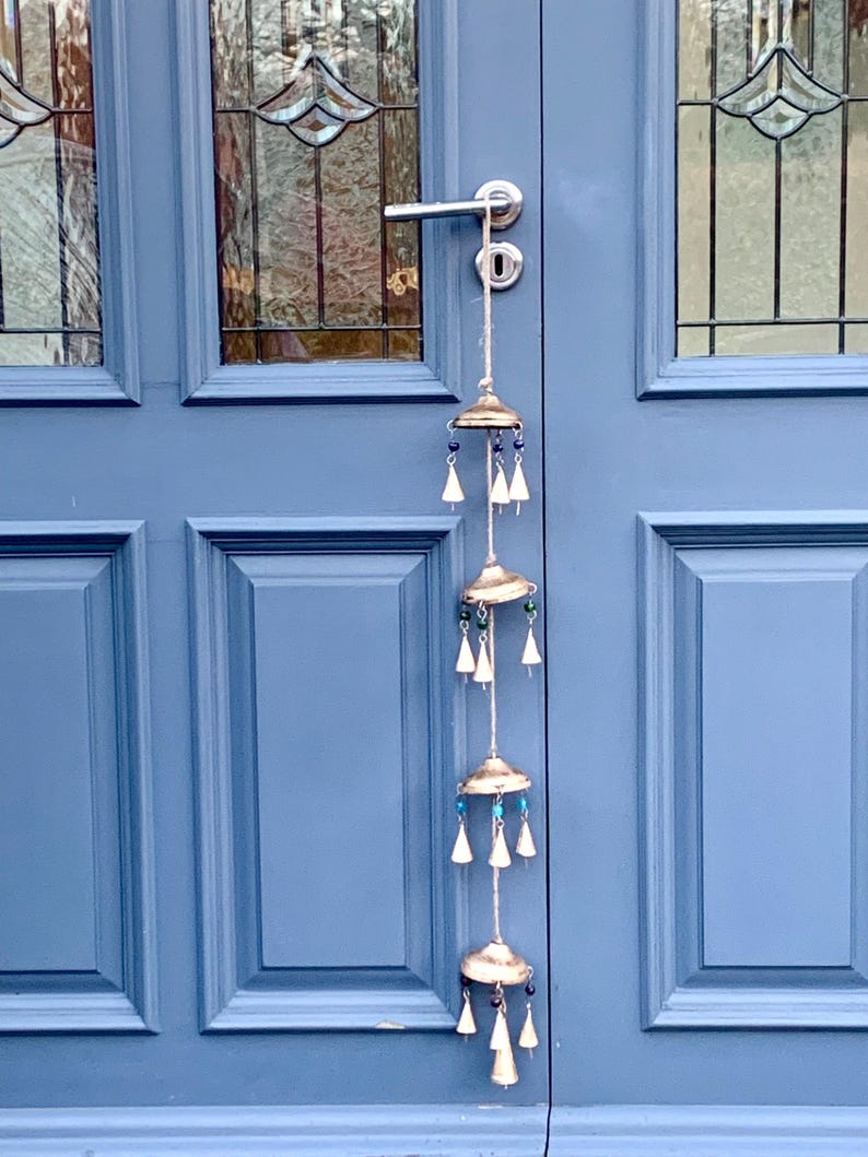 May include: A silver wind chime with five tiers of bells and beads hangs from a door handle. The bells are silver and the beads are blue, green, and white.