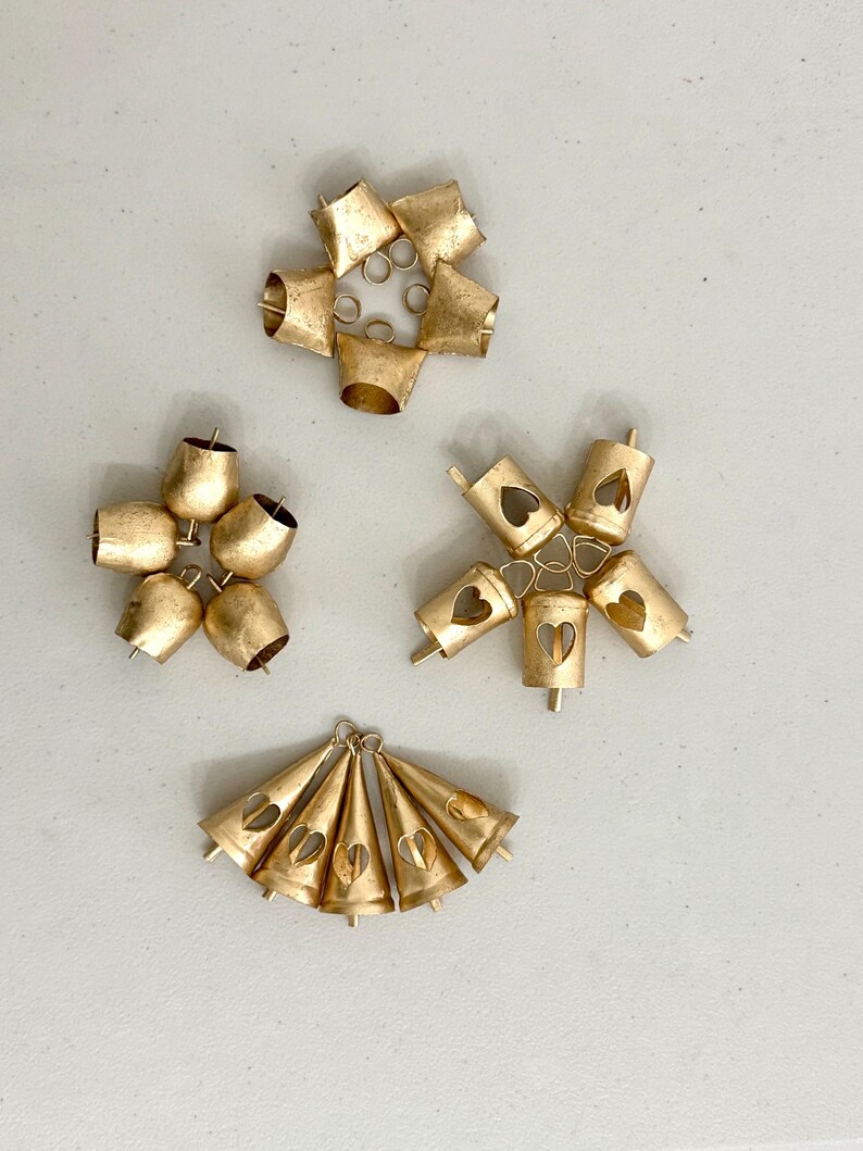 May include: An assortment of small, gold-colored bells in various arrangements. Some bells are clustered in circular shapes, while others are arranged in a fan-like pattern. Several bells feature heart-shaped cutouts.