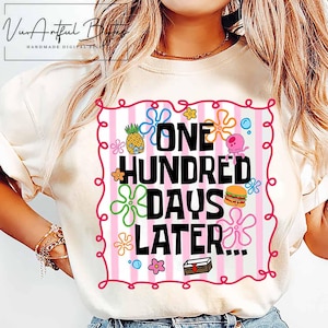 May include: Cream-colored t-shirt featuring the text "ONE HUNDRED DAYS LATER..." in black, with colorful cartoon graphics. The design includes a pineapple, flowers, a burger, and other playful elements within a pink and white striped frame.