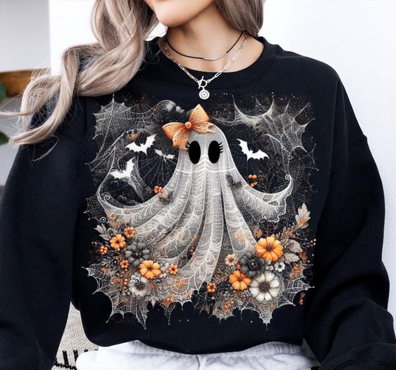Puede incluir: Sudadera negra con un dise&ntilde;o de fantasma de Halloween. El fantasma tiene un lazo, rodeado de telara&ntilde;as, murci&eacute;lagos y flores naranjas, blancas y grises. Un gr&aacute;fico festivo para la temporada.
