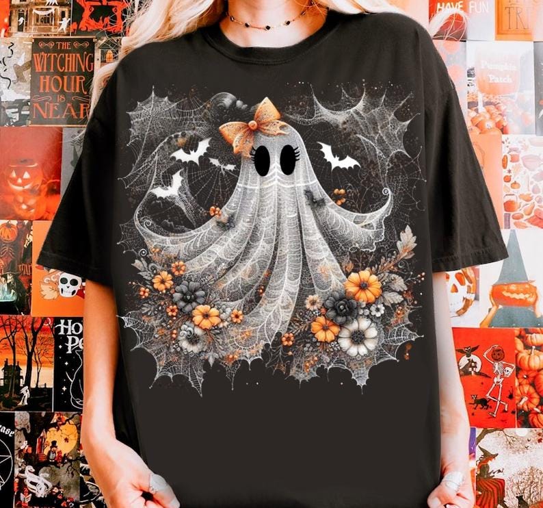 Puede incluir: Camiseta negra con un dise&ntilde;o caprichoso de fantasma con lazo, rodeado de telara&ntilde;as, murci&eacute;lagos y flores en naranja, amarillo y gris. El dise&ntilde;o tiene un tema de Halloween.