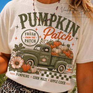May include: A cream-colored t-shirt featuring a graphic of a green vintage pickup truck loaded with orange pumpkins. The text reads PUMPKIN PATCH, FRESH FROM THE PATCH, FARM FRESH PUMPKINS, LOCALLY GROWN, PUMPKINS, CORN MAZE, and APPLE CIDER.