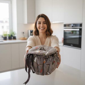 Könnte beinhalten: Eine runde Aufbewahrungstasche mit Kordelzug und dunkelbraunen Bändern. Die Tasche hat ein braunes und weißes Zickzackmuster mit farbigen Akzenten. Die Tasche wird vor einer weißen Küche gehalten.