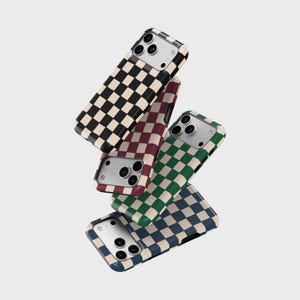 May include: Four smartphone cases arranged in a floating stack, each featuring a distinct checkered pattern. The colours include black and cream, maroon and cream, dark green and cream, and navy blue and cream, all with cutouts for camera lenses.