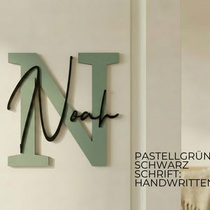May include: A wall-mounted wooden sign featuring the name "Noah" in a cursive font over a large letter "N". The letter "N" is a pastel green color, and the name "Noah" is black. The sign is mounted on a light-colored wall.