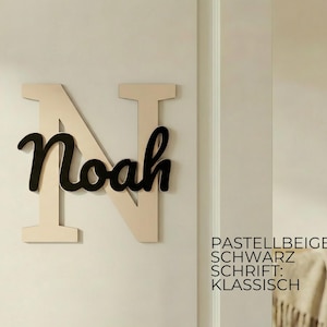 May include: A wooden wall decoration featuring the name "Noah" in black script over a large, light beige letter "N". The background is a light beige wall. The text on the right says "Pastellbeige, Schwarz, Schrift: Klassisch."