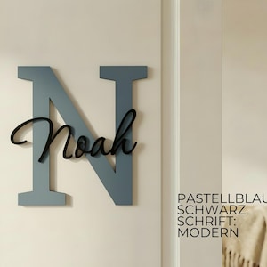 May include: A large, pastel blue wooden letter "N" with the name "Noah" in black script. The sign is mounted on a white wall. Text on the right reads "Pastellblau, Schwarz, Schrift: Modern."