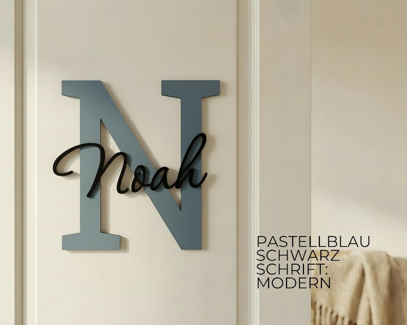 May include: A large, pastel blue wooden letter "N" with the name "Noah" in black script. The sign is mounted on a white wall. Text on the right reads "Pastellblau, Schwarz, Schrift: Modern."