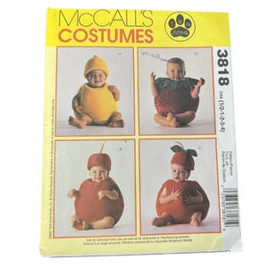 May include: McCall's Costumes pattern 3818 featuring Tom Arma designs for infants. The yellow envelope displays four fruit-themed costumes: a yellow lemon, a red strawberry, a red cherry, and a red apple, each worn by a baby in a studio setting.