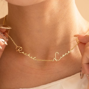 Puede incluir: Un delicado collar dorado con los nombres "Rachel" y "Liana" en cursiva. El collar es sostenido por una persona, mostrando el diseño y los finos detalles de la cadena. Los nombres están conectados por una fina cadena.