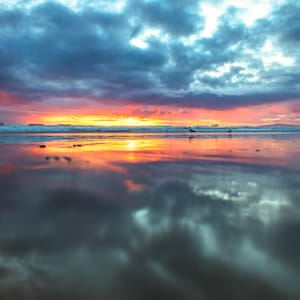 Puede incluir: Una colorida puesta de sol sobre un océano tranquilo con un reflejo del cielo en el agua.