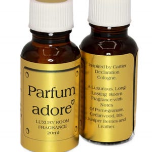 May include: Two 20ml brown glass bottles with gold labels.  The labels on the bottles feature the text 'Parfum adore', 'Luxury Room Fragrance', and  'Inspired by Cartier Declaration Cologne.'  The back label lists fragrance notes including pomegranate, cedarwood, iris, juniper berries, and leather.