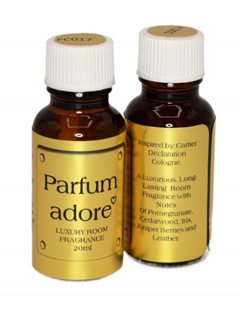 May include: Two 20ml brown glass bottles with gold labels.  The labels on the bottles feature the text 'Parfum adore', 'Luxury Room Fragrance', and  'Inspired by Cartier Declaration Cologne.'  The back label lists fragrance notes including pomegranate, cedarwood, iris, juniper berries, and leather.
