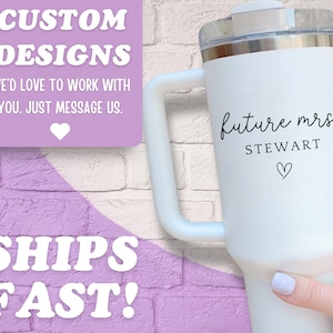 Puede incluir: Vaso t&eacute;rmico blanco con asa, con el texto "future mrs. STEWART" y un s&iacute;mbolo de coraz&oacute;n. El vaso tiene una tapa transparente y se sostiene contra un fondo de pared de ladrillo. La imagen tambi&eacute;n incluye el texto "CUSTOM DESIGNS" y "SHIPS FAST!"