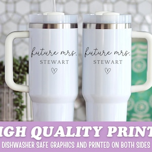 Puede incluir: Dos tazas de viaje blancas con bordes plateados y asas blancas. Cada taza tiene el texto "future mrs. STEWART" y un s&iacute;mbolo de coraz&oacute;n negro. Las tazas est&aacute;n sobre un fondo blanco.