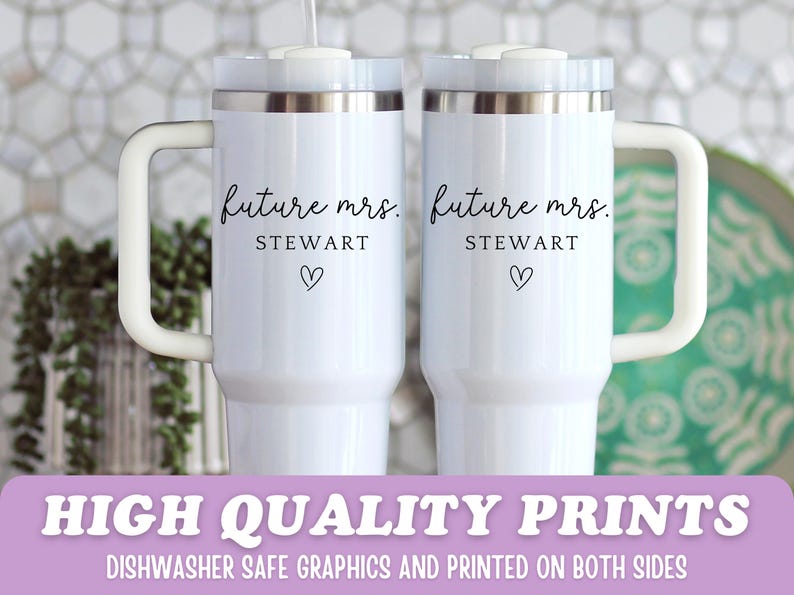 Puede incluir: Dos tazas de viaje blancas con bordes plateados y asas blancas. Cada taza tiene el texto "future mrs. STEWART" y un s&iacute;mbolo de coraz&oacute;n negro. Las tazas est&aacute;n sobre un fondo blanco.