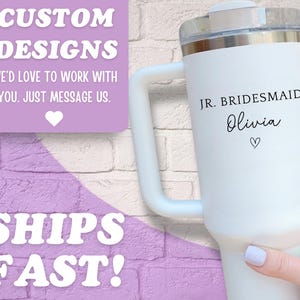 Pu&ograve; includere: Bicchiere termico bianco con manico, personalizzato con "JR. BRIDESMAID Olivia" e un cuore. Il bicchiere ha un coperchio trasparente ed &egrave; contro uno sfondo di muro di mattoni. Il testo sull'immagine dice "CUSTOM DESIGNS" e "SHIPS FAST!"