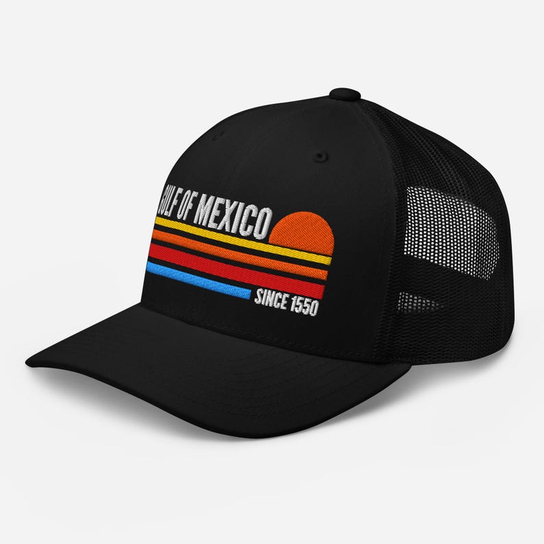 May include: Black trucker hat with a mesh back and a curved brim. The front features the text "GULF OF MEXICO" above a colorful sunset design with the text "SINCE 1550". The hat is a classic accessory.