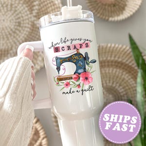 May include: White tumbler with a handle, featuring a sewing machine design and the text "when life gives you scraps make a quilt". The design includes pink flowers and the name "Christine".