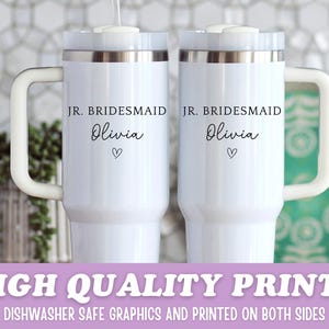 Pu&ograve; includere: Due tazze da viaggio bianche con bordi argentati e manici bianchi. Ogni tazza ha il testo "JR. BRIDESMAID Olivia" con un simbolo a forma di cuore. La parte inferiore dell'immagine ha il testo "HIGH QUALITY PRINTS" e "DISHWASHER SAFE GRAPHICS AND PRINTED ON BOTH SIDES".