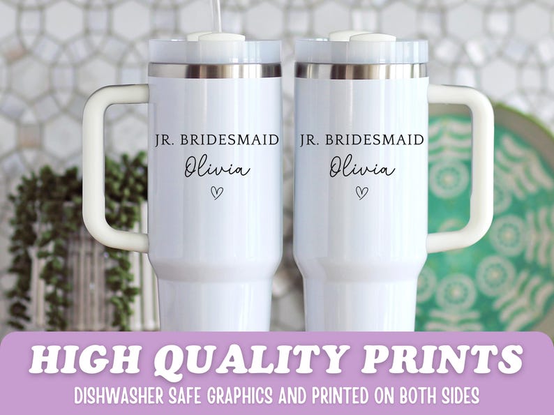 Pu&ograve; includere: Due tazze da viaggio bianche con bordi argentati e manici bianchi. Ogni tazza ha il testo "JR. BRIDESMAID Olivia" con un simbolo a forma di cuore. La parte inferiore dell'immagine ha il testo "HIGH QUALITY PRINTS" e "DISHWASHER SAFE GRAPHICS AND PRINTED ON BOTH SIDES".