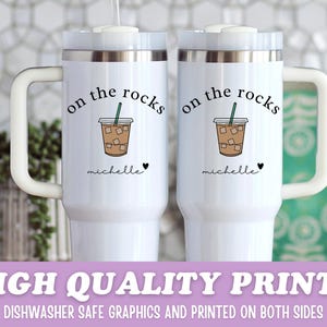 May include: Two white travel mugs with handles, each featuring the text "on the rocks" above a graphic of an iced coffee. Below the graphic is the name "michelle" and a heart. The bottom of the image reads "HIGH QUALITY PRINTS".
