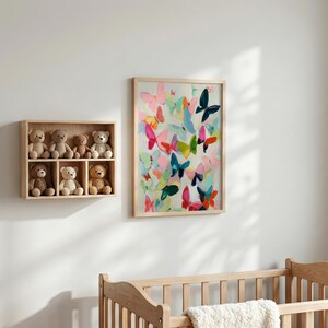 May include: A colourful butterfly art print in a light wood frame adorns a white wall. The artwork showcases butterflies in pink, blue, green, and orange. A wooden shelf with six teddy bears is positioned to the left.