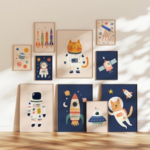 Op de afbeelding: Een verzameling ingelijste kunstprints met ruimte-thema illustraties. De kunstwerken bevatten raketten, planeten, astronauten, een kat in een ruimtepak en een UFO. Het kleurenpalet omvat blauw, oranje en crème.