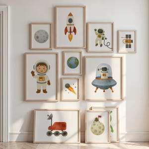 Könnte beinhalten: Eine Sammlung gerahmter Kunstdrucke mit Weltraum-Illustrationen. Die Kunstwerke zeigen eine Rakete, einen Astronauten, den Mond, die Erde, einen Kometen, einen Satelliten, einen Weltraumrover und einen Astronauten in einem UFO. Die Drucke sind in Holzrahmen.