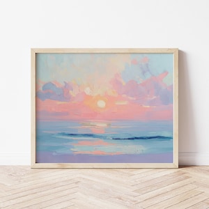 May include: A framed painting depicting a sunset over the sea. The artwork uses a vivid palette of pink, orange, and blue tones. The sun is a bright disc, and the water mirrors the sky's colours. The painting is in a light-coloured wooden frame.