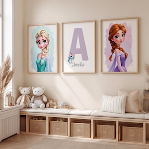 May include: Three framed art prints featuring cartoon characters. One print shows a blonde woman in a teal dress, another displays a large purple letter "A" with the name "Amelia", and the third depicts a woman with red hair in a purple dress.