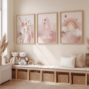 Puede incluir: Tres impresiones enmarcadas con un unicornio, una letra "A" con el nombre "Amelia" y un arcoíris. Las impresiones tienen una combinación de colores rosa y dorado. La habitación también cuenta con un banco con cestas de almacenamiento y osos de peluche.