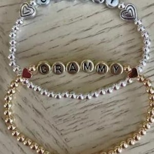 May include: Two bracelets with the word "GRAMMY" spelled out in silver and gold beads. Both bracelets have small heart charms on either side of the word.