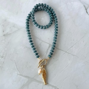 Peut inclure: Collier de perles turquoise avec fermoir dor&eacute; et pendentif poisson. Le collier est dot&eacute; d'un fermoir &agrave; bascule et d'une petite perle rose clair. Les perles sont d'un bleu-vert profond.
