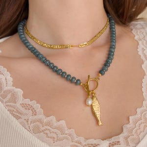 Peut inclure: Ensemble de deux colliers. La cha&icirc;ne sup&eacute;rieure est en or. Le collier inf&eacute;rieur est un collier de perles avec un pendentif poisson dor&eacute; et une perle. Les perles sont de couleur bleu-vert. Le pendentif poisson est dor&eacute;.