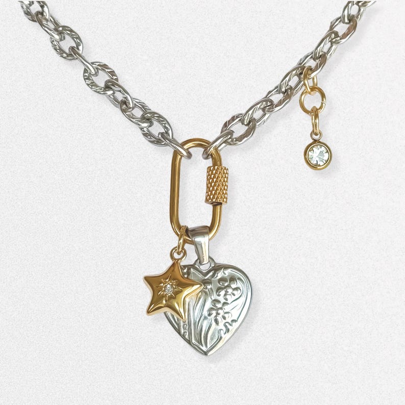 May include: Silver-tone chain necklace with a gold-tone clasp and charms. The charms include a gold star with a small diamond, a silver heart with floral detailing, and a small gold charm with a clear crystal. The necklace is on a white background.