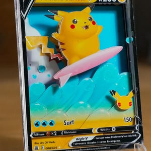 May include: Pikachu Surfeur V Pokemon card featuring a yellow Pikachu riding a pink surfboard on a blue wave. The card has a black border and a white background. The card is a holographic card with a 3D effect. The card is a rare card with a value of 200. The card is a part of the Sword & Shield series.