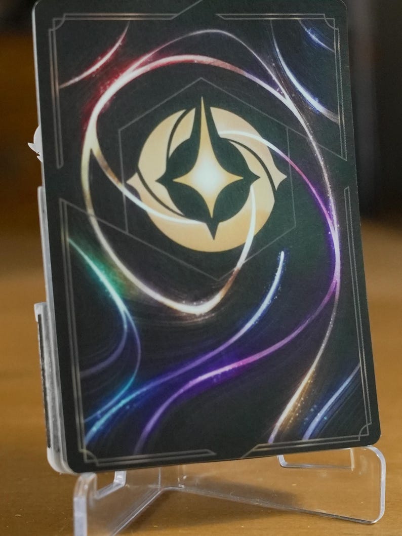 May include: Close-up view of a card with a dark background featuring swirling, multicolored neon lines. A central, light beige hexagonal emblem with a glowing, four-pointed star is prominently displayed. The card is displayed on a clear acrylic stand. The overall aesthetic suggests a fantasy or mystical theme.