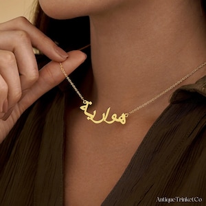 May include: A gold-colored necklace with an Arabic name pendant. The pendant features the name "Hawa" in elegant script. The necklace is displayed against a neutral background, highlighting the jewelry's design and color.
